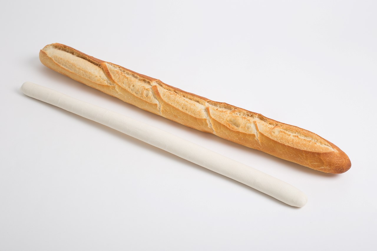 Une baguette à côté d'un objet long, blanc et roulé, probablement de la pâte