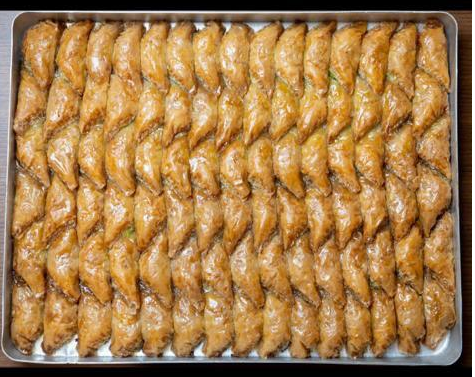 Plateau de pâtisseries baklava dorées, disposées en rangées torsadées.