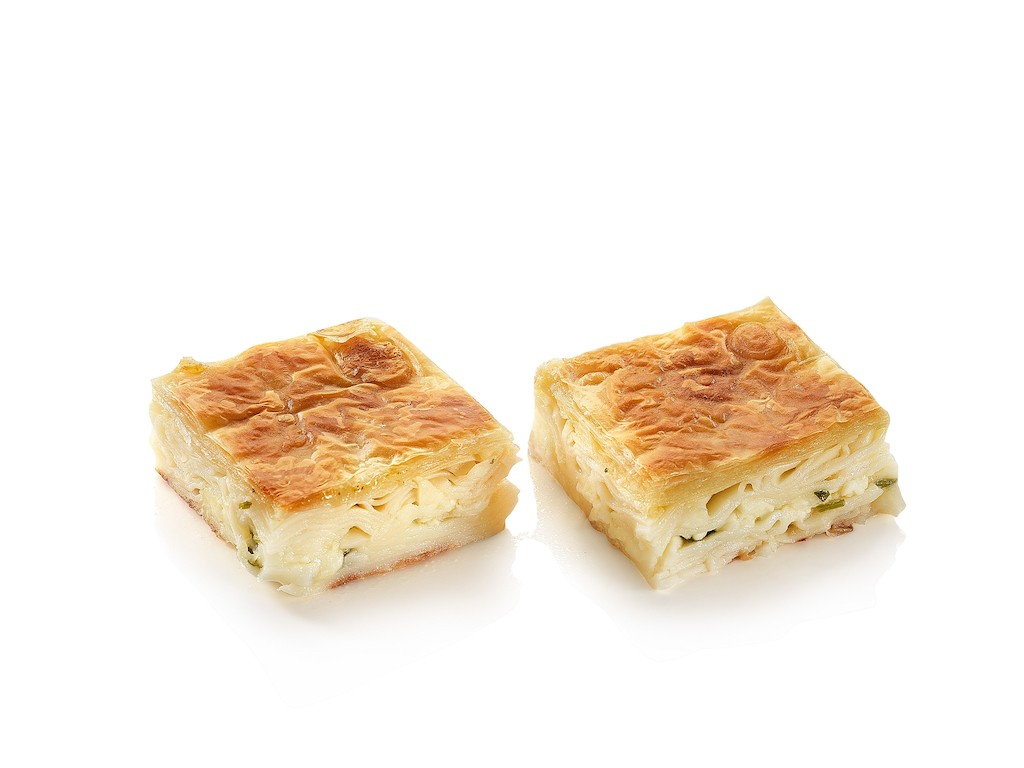 Deux pâtisseries salées carrées, dorées et fourrées d'une crème blanche sur un fond blanc.