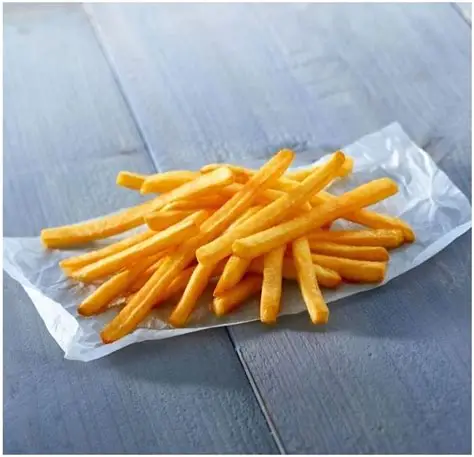 Pile de frites dorées sur du papier blanc, posée sur une surface en bois gris.