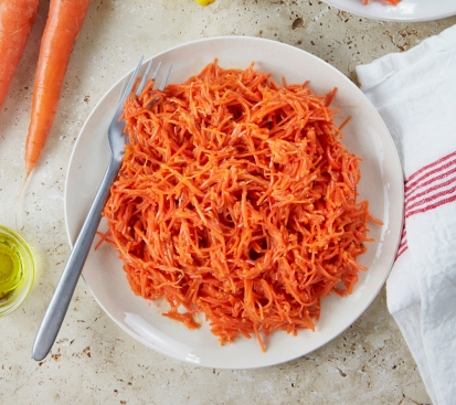 Assiette de carottes râpées avec une fourchette sur une surface claire.