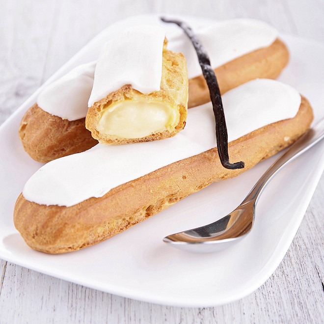 Éclairs à la vanille nappés de glaçage blanc, présentés sur une assiette blanche.
