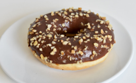 Beignet glacé au chocolat avec des noix hachées, servi sur une assiette blanche.