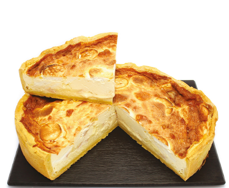 Quiche sur une assiette carrée noire avec une part découpée, croûte et garniture légèrement dorées.