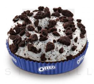 Beignet Oreo avec glaçage blanc et miettes de biscuits, dans un support en papier Oreo bleu.