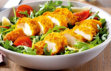 Salade de poulet avec du poulet pané, des tomates et de la roquette dans un bol blanc.