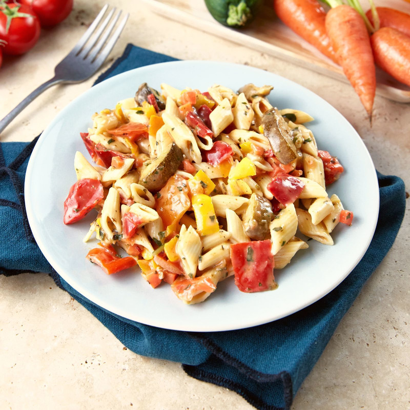 Salade de pâtes aux tomates, poivrons et courgettes sur une assiette blanche