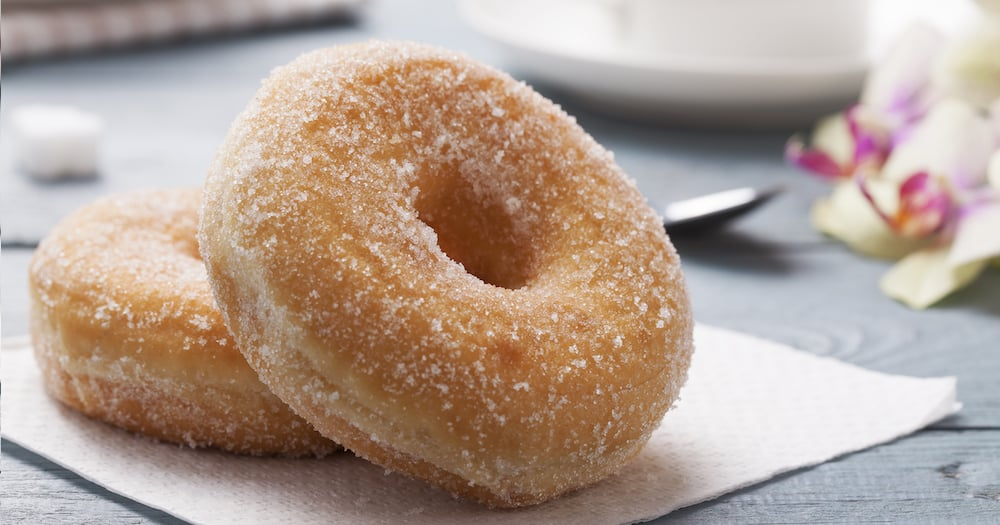 Deux beignets enrobés de sucre sur une serviette blanche, avec une tasse de café et une orchidée en arrière-plan.