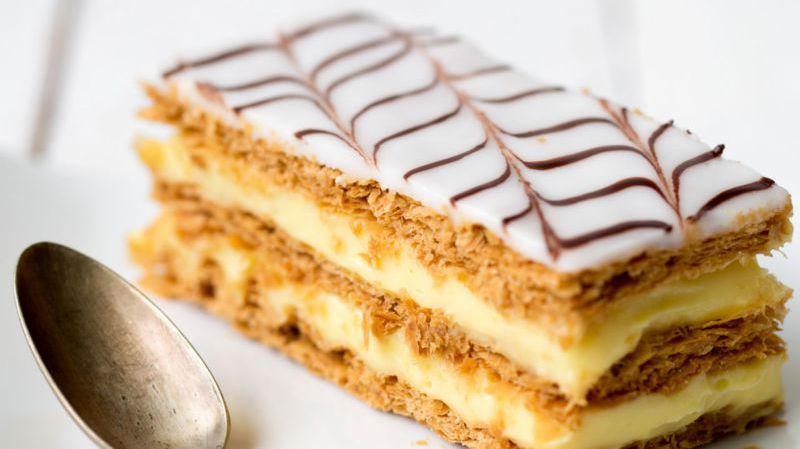 Gâteau Napoléon fourré à la crème, recouvert d'un glaçage blanc et de filets de chocolat.