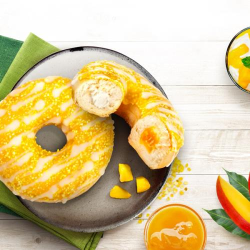 Deux beignets à la mangue sur une assiette, garnis de mangue, accompagnés d'un smoothie à la mangue, sur une table en bois.