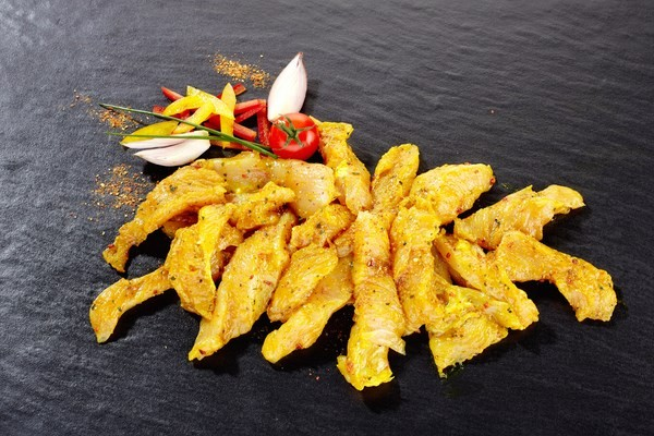 Lanières de poulet assaisonnées d'épices, servies sur une ardoise noire et garnies de légumes.