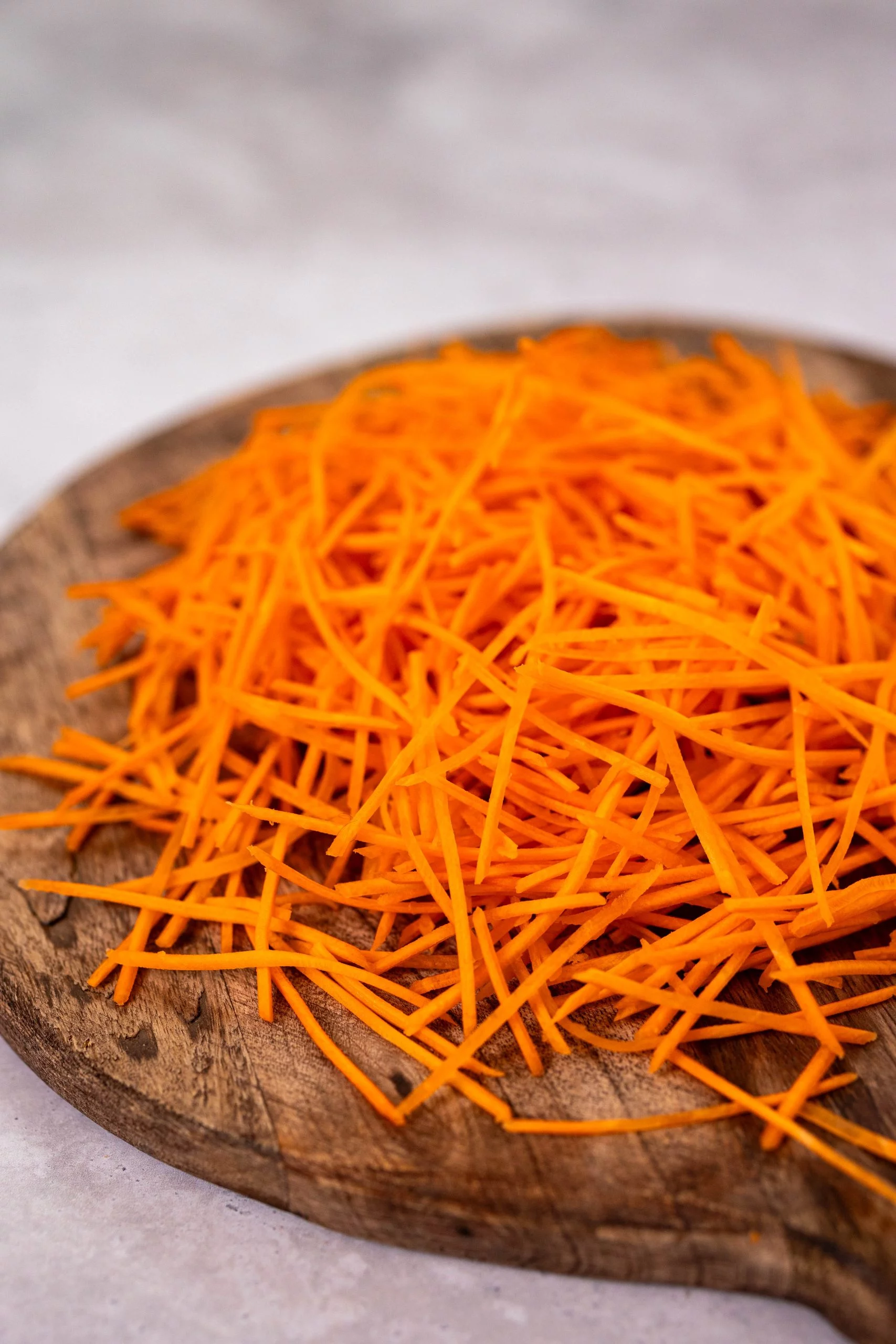 Carottes râpées sur une planche à découper en bois, sur fond gris clair.