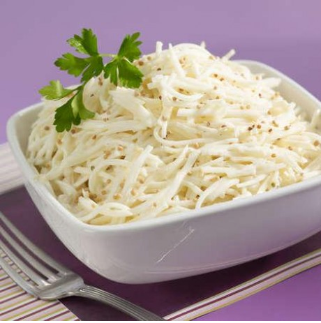 Salade de céleri-rave râpé dans un bol blanc, sauce crémeuse, graines et persil. Fond violet.