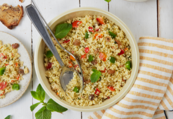 Salade de couscous dans un bol avec une cuillère, entourée de feuilles de menthe,