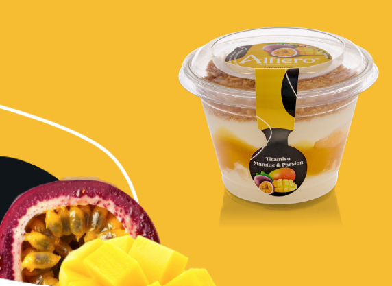 Coupe à dessert composée de couches de mangue, de fruit de la passion et de crumble, sur fond jaune.