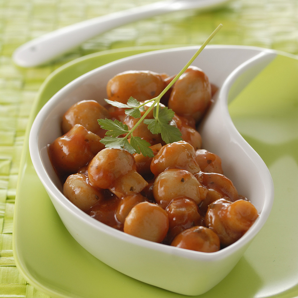 Champignons en sauce dans un bol blanc incurvé, posé sur une assiette verte.