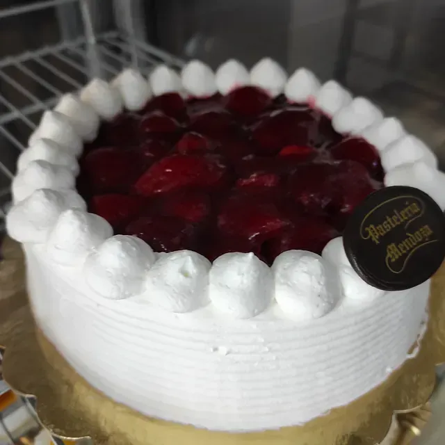Un pastel blanco con cerezas encima y una etiqueta que dice pasteleria