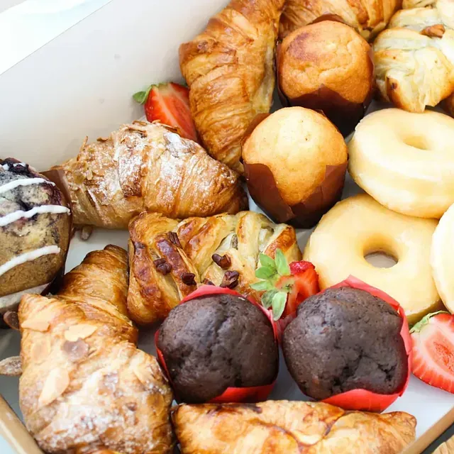 Una caja llena de una variedad de pasteles, incluidos croissants y donas.