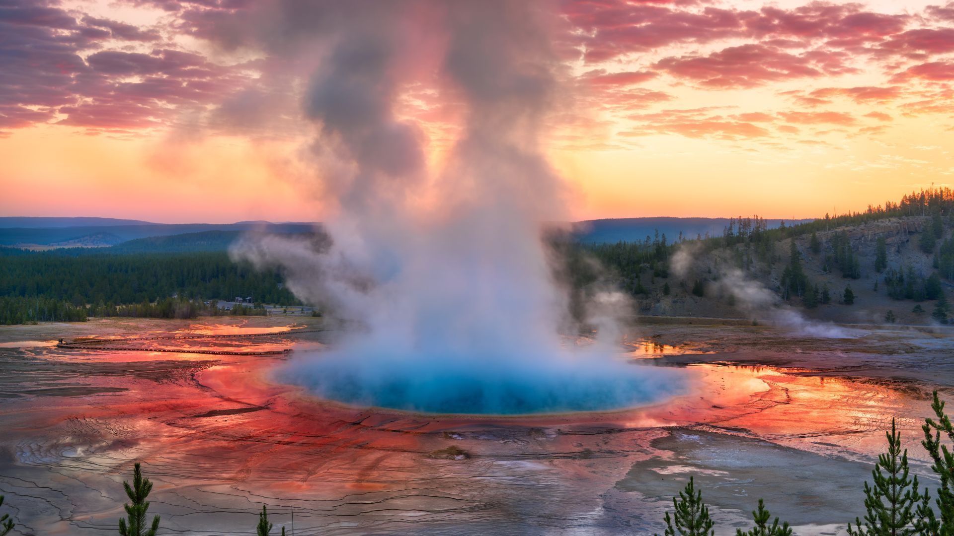 A geyser is erupting into the water at sunset.