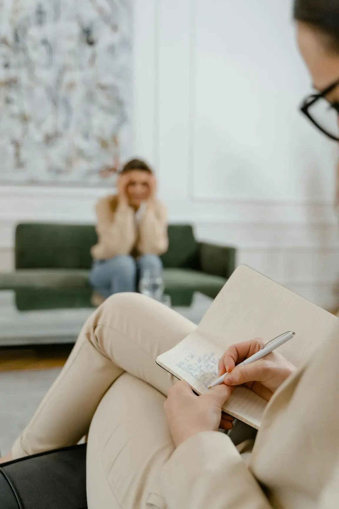 Terapeuta tomando notas mientras un paciente está sentado en un sofá en un consultorio de terapia.