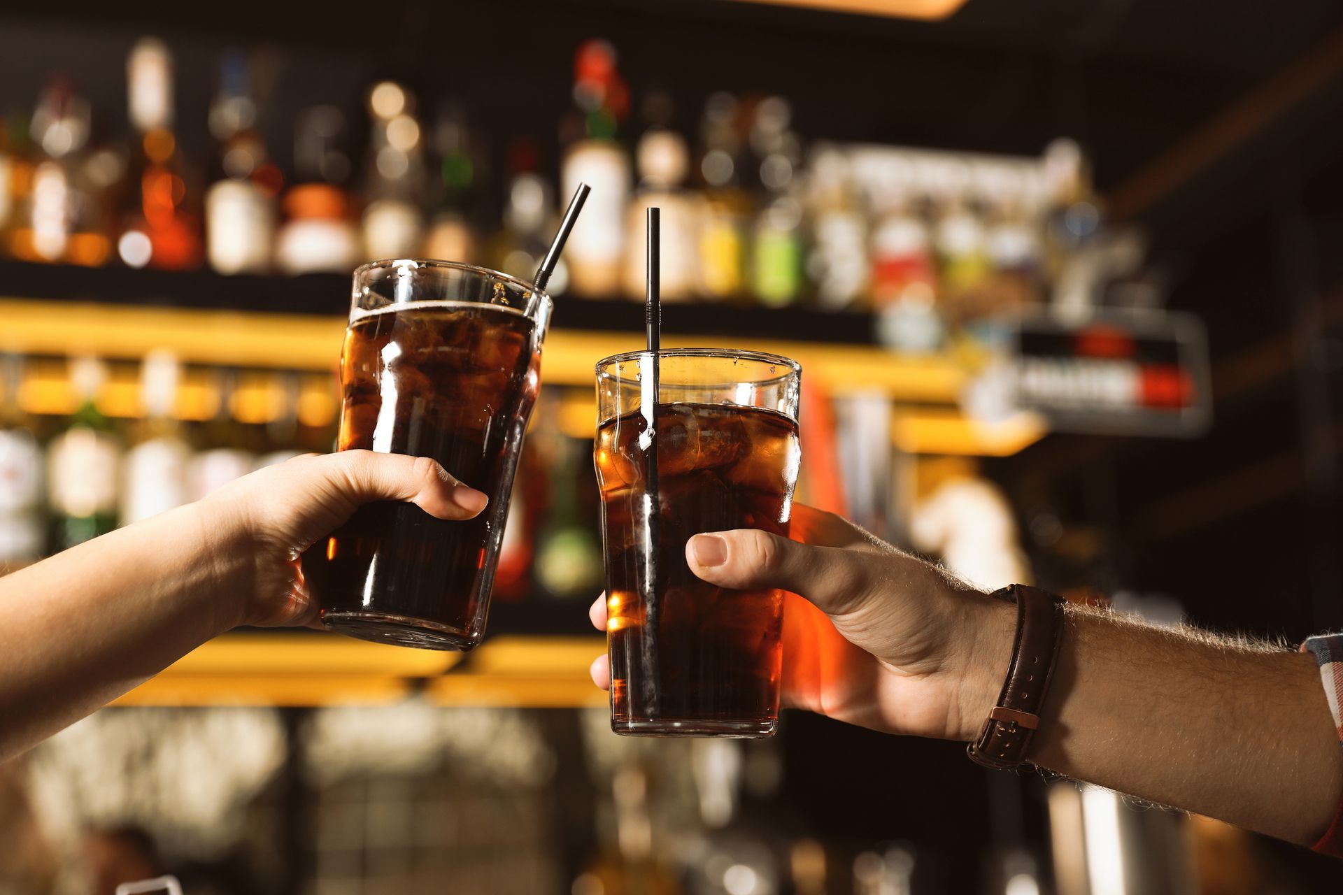 Dos personas brindan con vasos de refresco en un bar.