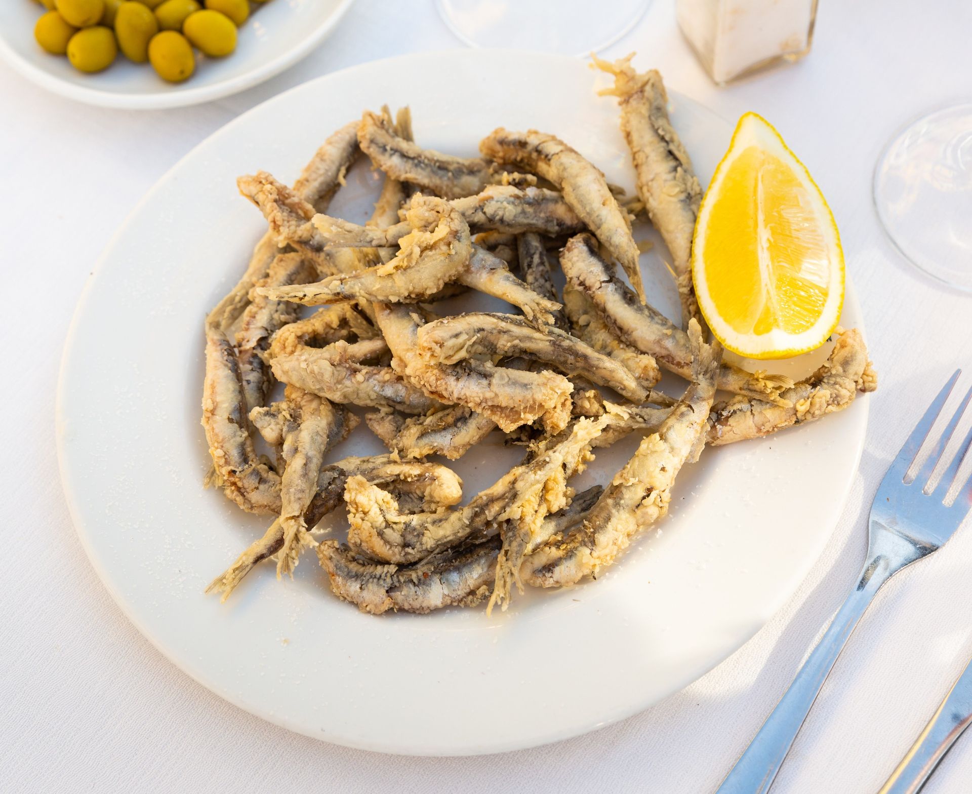 Un plato blanco cubierto con pescado frito y una rodaja de limón.