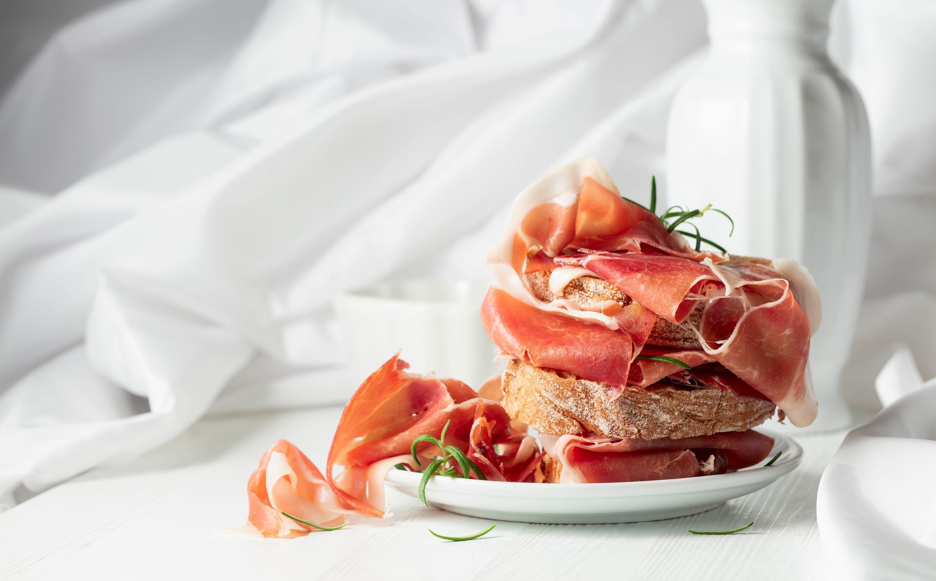 Un sándwich con jamón en un plato blanco sobre una mesa.