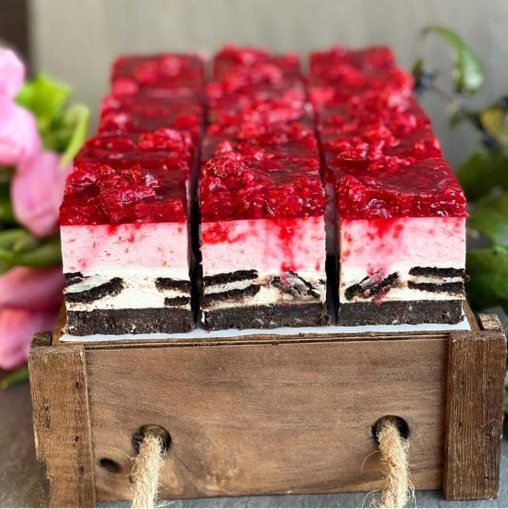Una caja de madera llena de rebanadas de tarta de queso y frambuesa.