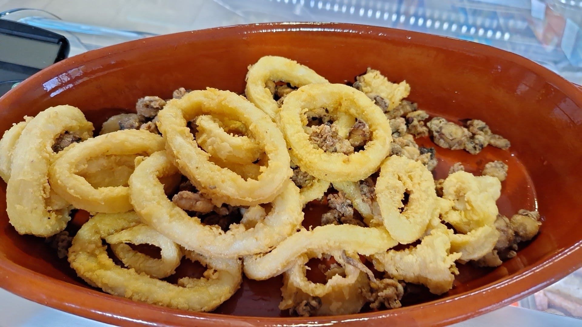 Un bol de aros de cebolla fritos y carne sobre una mesa.