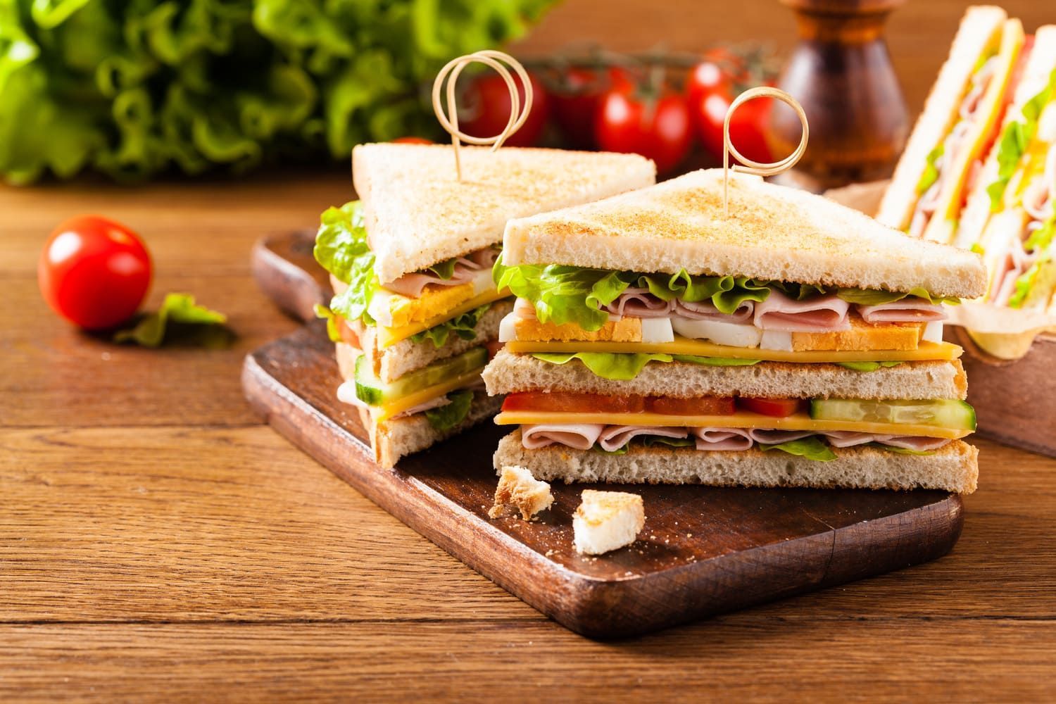 Un sándwich club se apila uno encima del otro sobre una tabla de cortar de madera.