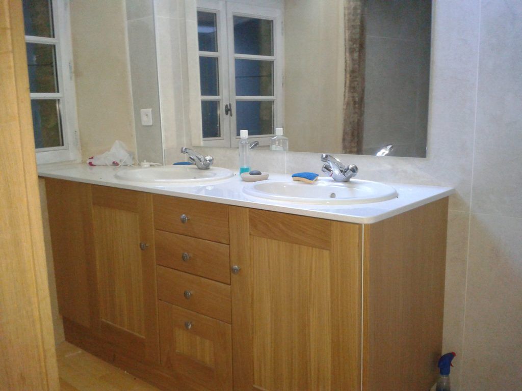 Meuble-lavabo de salle de bain avec un plan de travail blanc, des armoires en bois et un mur miroir.