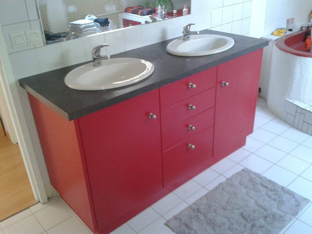 Meuble-lavabo rouge avec deux vasques et un plan de toilette gris, à côté d’une douche carrelée.