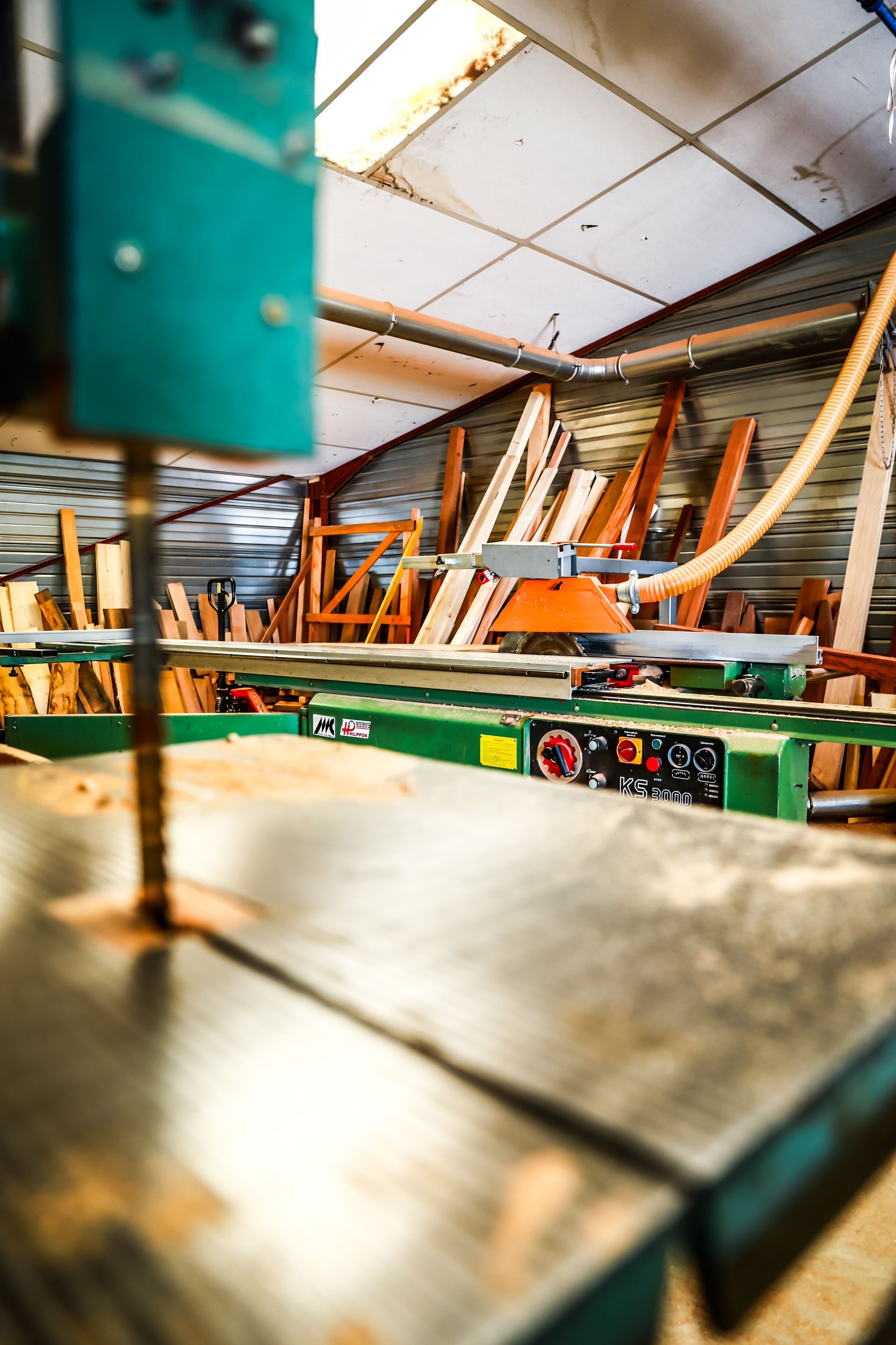 Atelier de menuiserie avec des scies, du bois et des machines sous un toit en métal