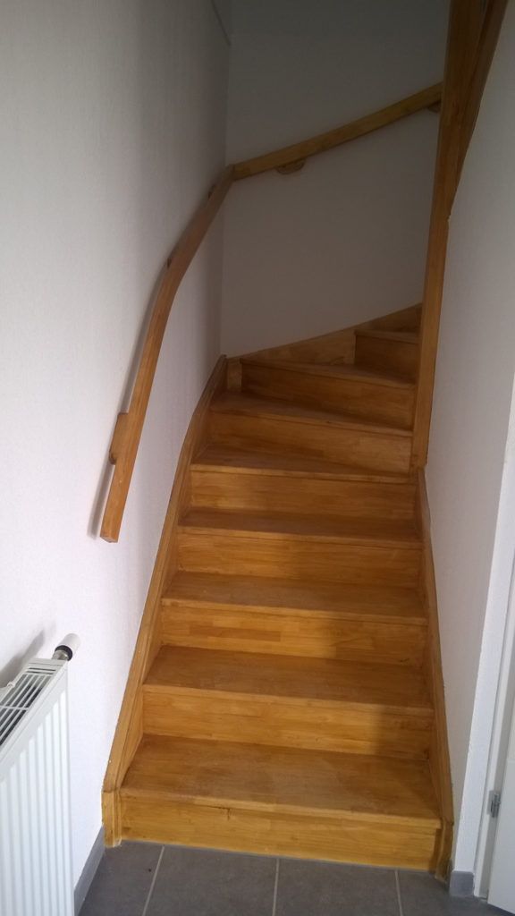 Escalier intérieur étroit avec des marches en bois et une rampe le long du mur de gauche