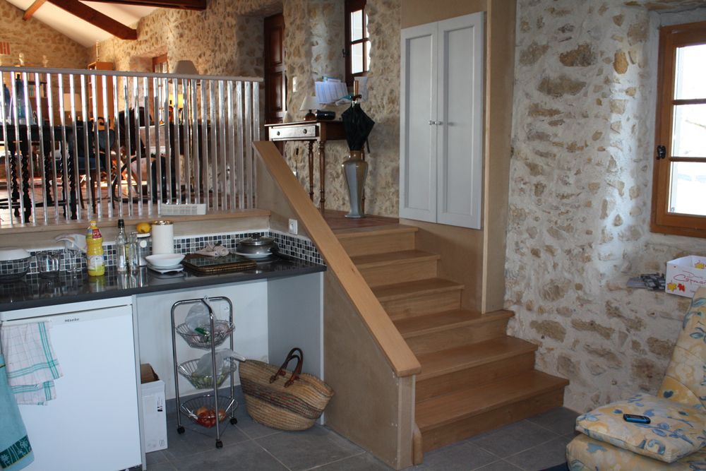 Intérieur de cuisine en pierre avec un comptoir, un escalier, des poutres en bois et une porte blanche