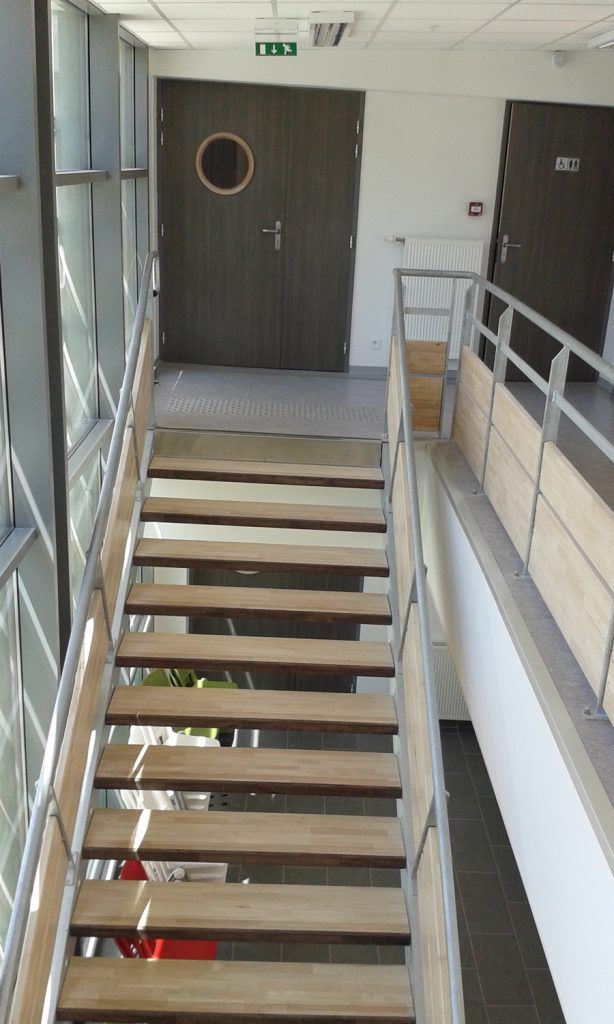 Cage d’escalier intérieure avec un escalier étroit menant à une porte marron et une rampe sur la droite