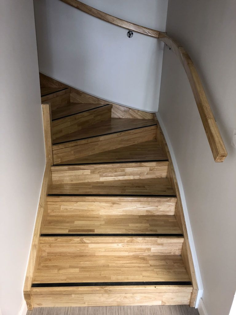 Escalier en bois avec une rampe dans un couloir intérieur étroit, vu d’en bas vers le haut.