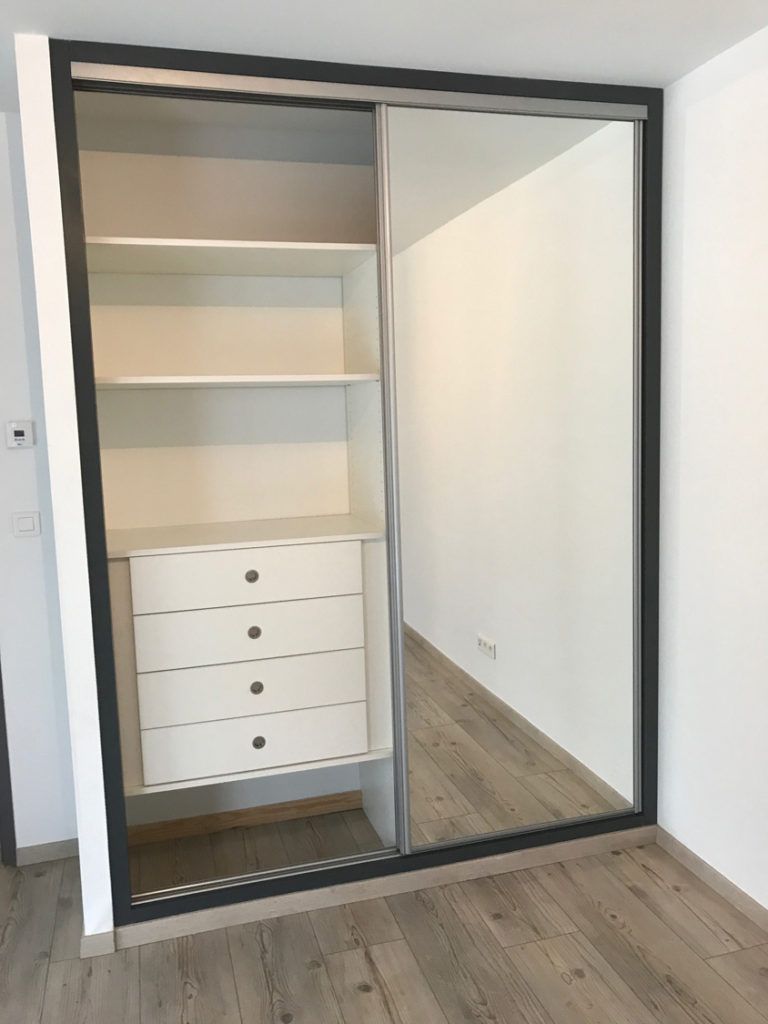 Placard ouvert avec des étagères, des tiroirs et une porte coulissante miroir dans une pièce moderne.