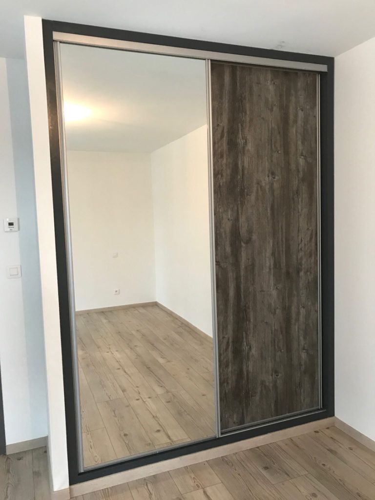 Porte de placard coulissante à miroir avec panneau en bois foncé dans une pièce presque vide