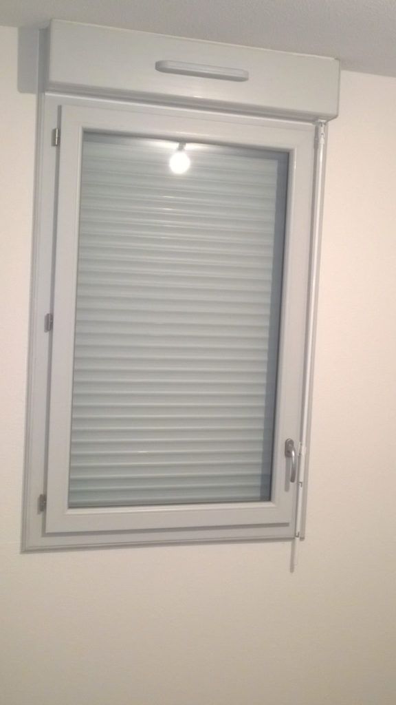 Fenêtre blanche avec des stores fermés et un cordon de tirage sur un mur beige