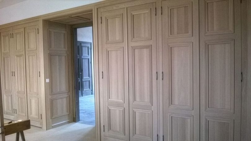 Des portes de placard en bois intégrées bordent un couloir, avec une porte ouverte donnant sur une pièce bleue.