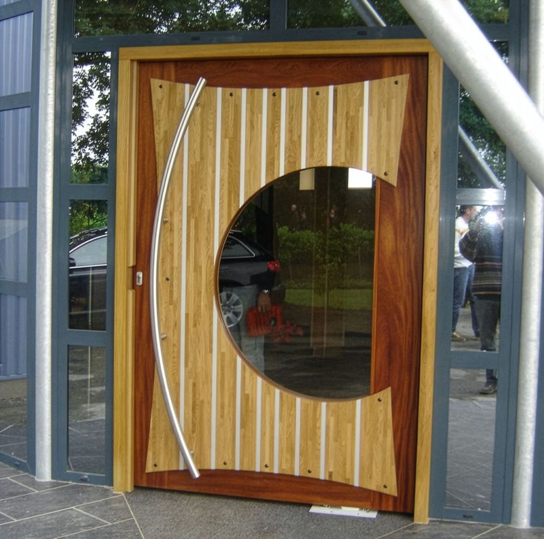 Porte en bois avec une grande fenêtre circulaire en verre, à l’entrée d’un bâtiment moderne vitré