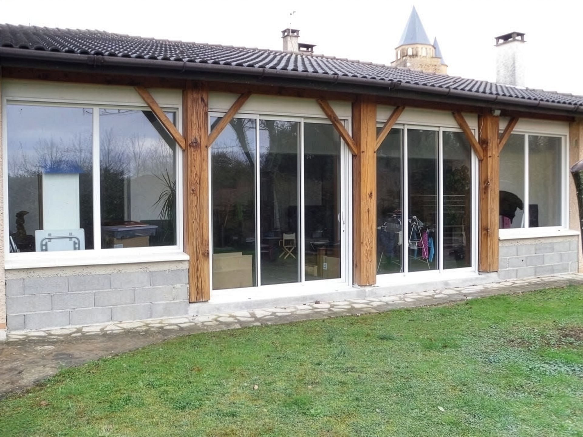 Extérieur d'une maison moderne avec de grandes fenêtres, des poteaux en bois et une pelouse