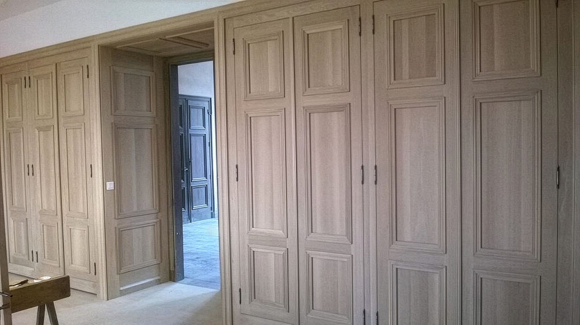 Mur de placards encastrés en bois clair, avec des portes à panneaux et une porte ouverte dans une pièce lumineuse