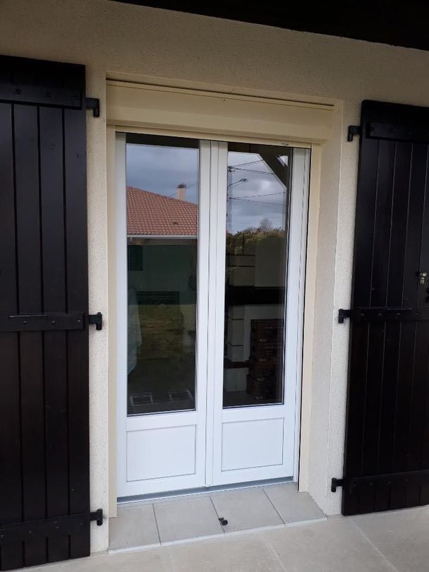 Portes-fenêtres blanches à double battant, avec des volets noirs de chaque côté, vues de l’extérieur.