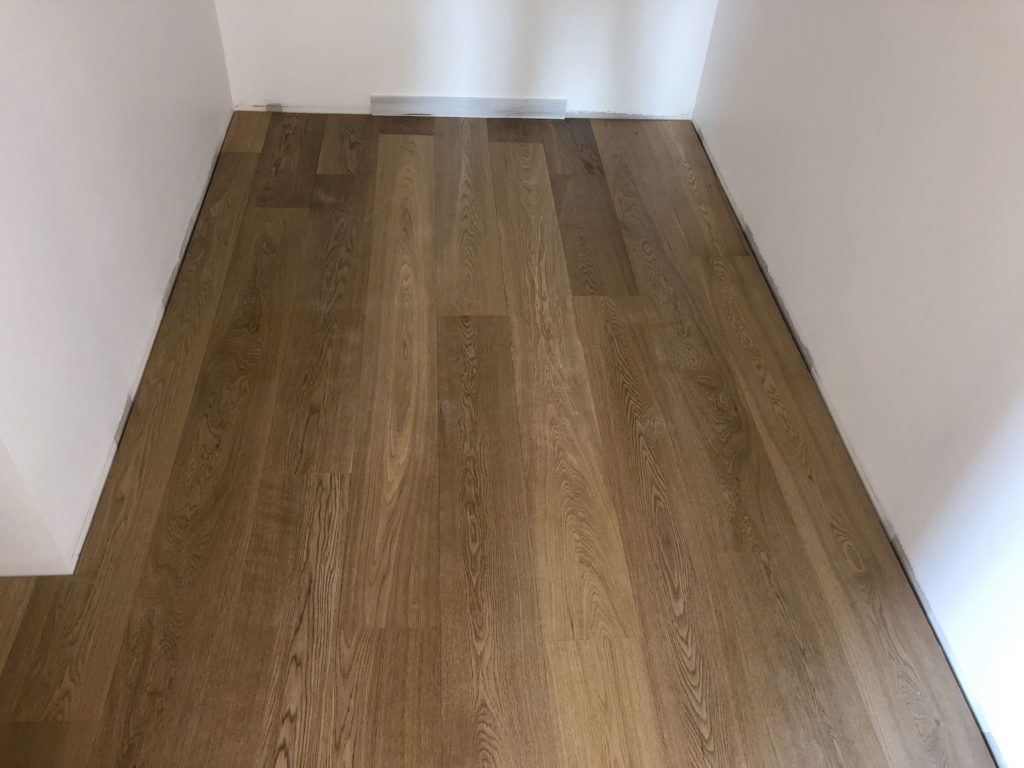 Pièce étroite et vide, avec un parquet clair et des murs blancs