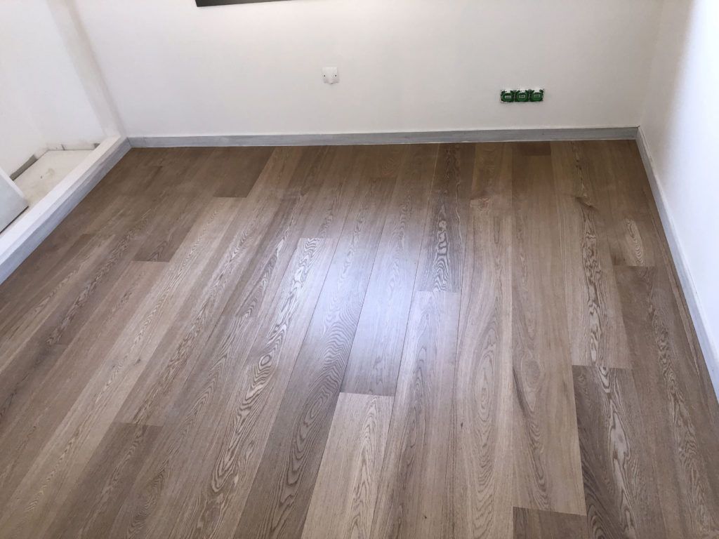 Pièce vide avec un parquet clair, des murs blancs, une prise électrique et une sortie de câble visibles.