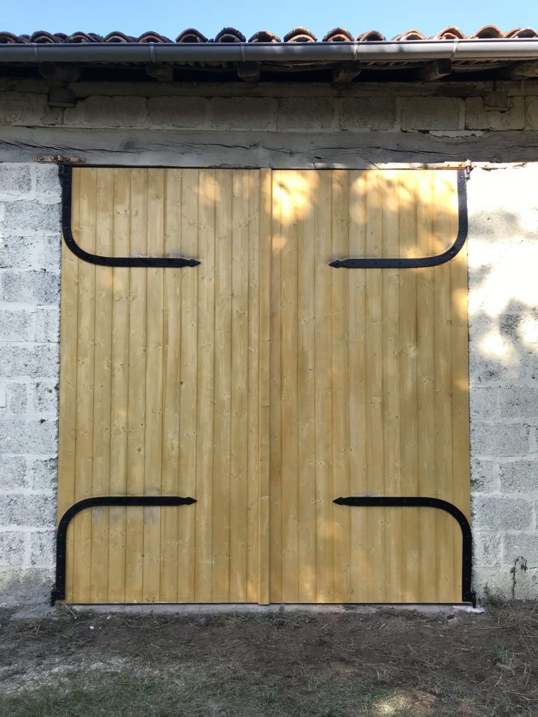 Ensemble de deux portes de garage en bois dans un mur en béton gris, avec un toit en tuiles rouges au-dessus.