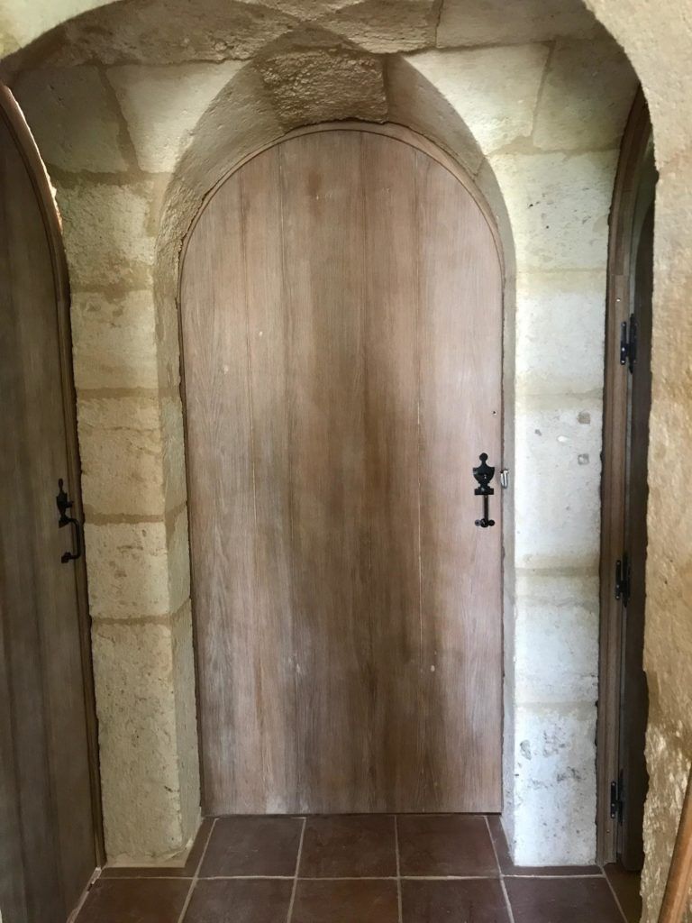 Porte cintrée en bois dans un couloir en pierre avec un sol carrelé