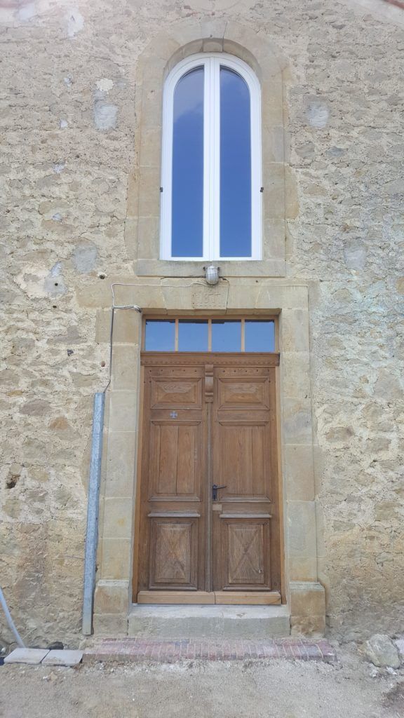 Façade en pierre avec une fenêtre cintrée au-dessus d’une porte en bois et des marches